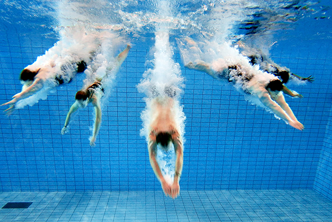 Bild på fem personer som dyker ner i en bassäng.