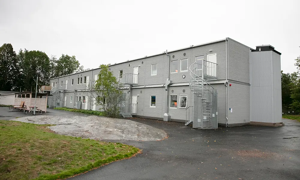 Foto på Enögla förskola. Det är en grå barackbyggnad med flera våningar.